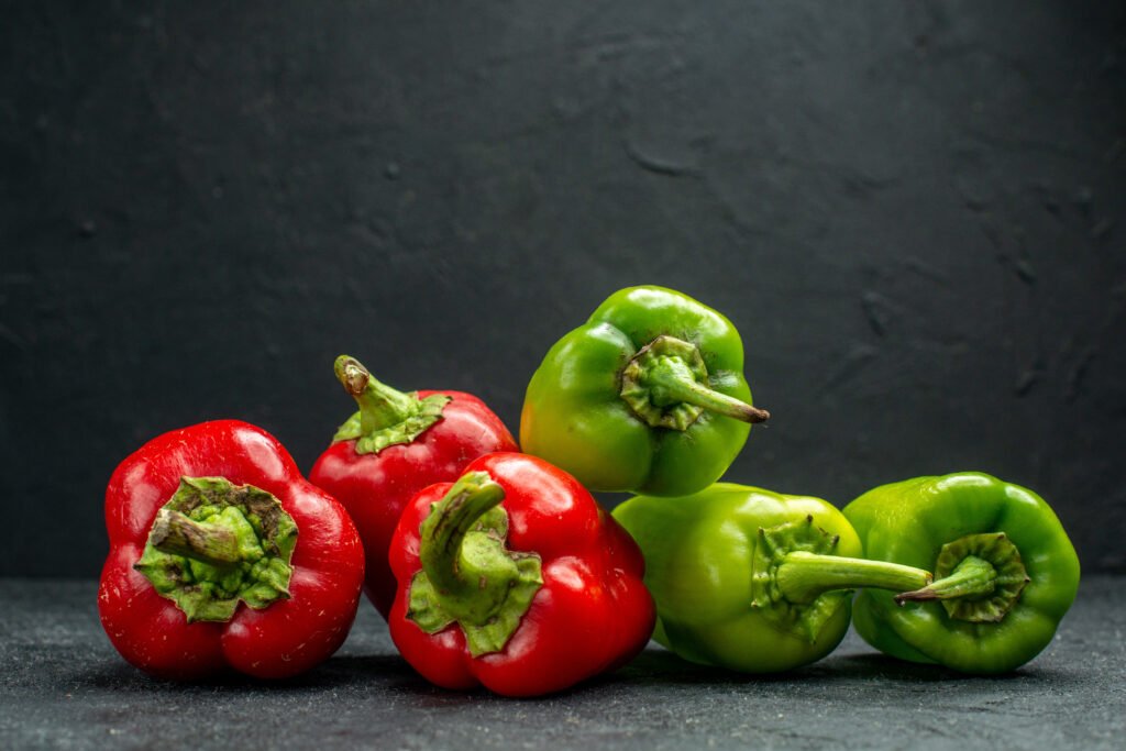 side view green red bell peppers dark green table dark grey background