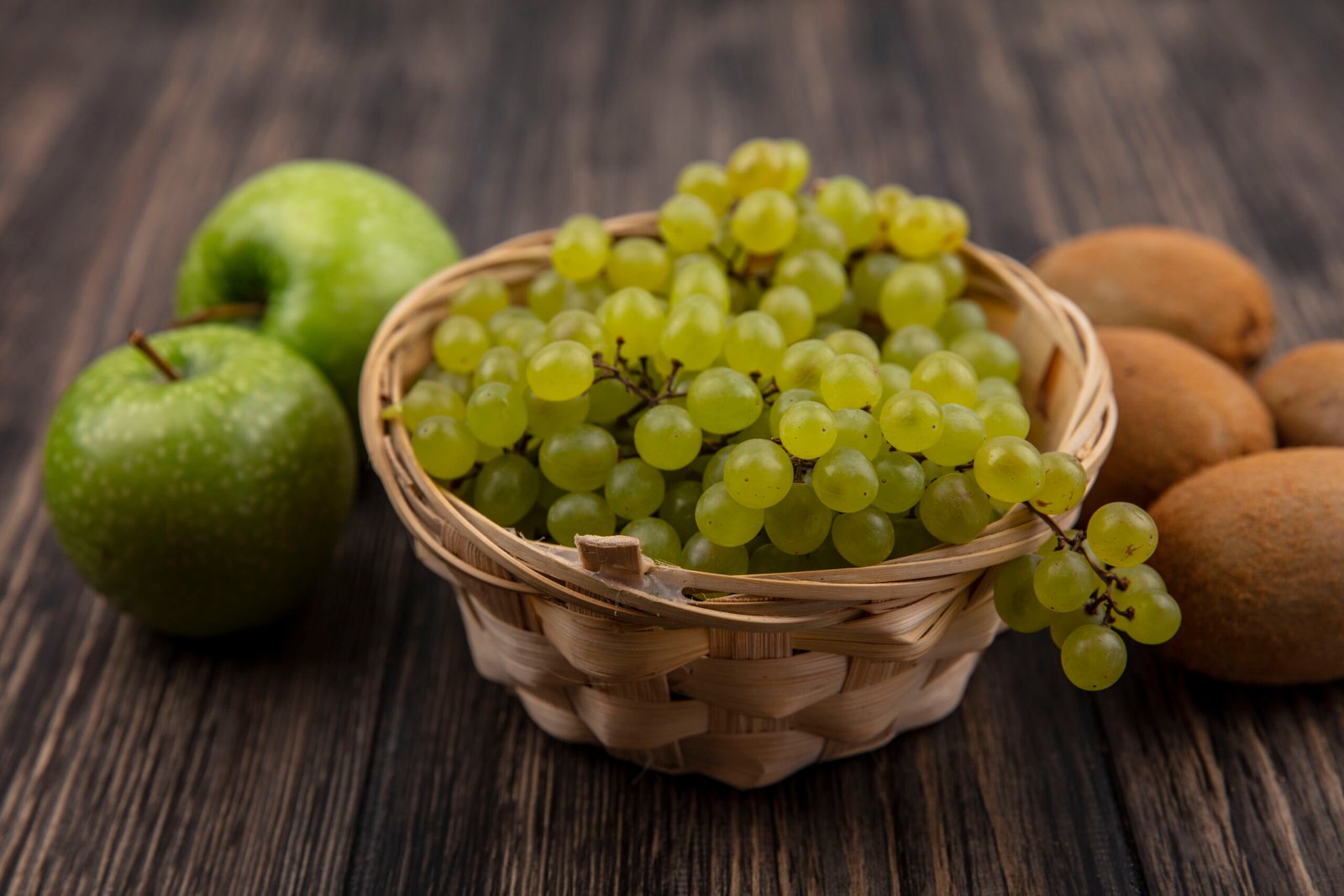 front view green grapes in a basket with green apples and kiwi on a wooden background